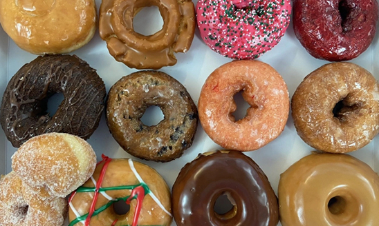 A dozen donuts, all different types, flavors and icing styles, viewed from above