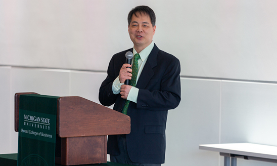 Hayong Yun standing at a podium to welcome attendees to the Investment Celebration event