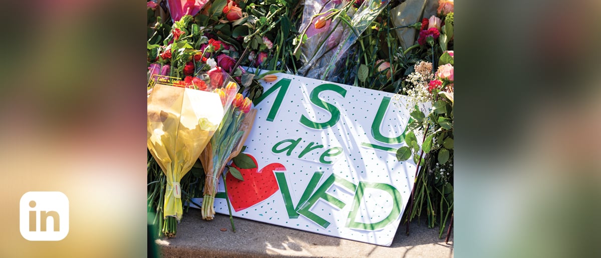 A handmade sign reading MS*U* Are Loved, surrounded by bouquets of flowers