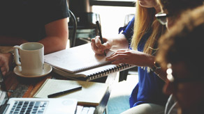 A group of people gather for a meeting, taking notes, in a casual setting