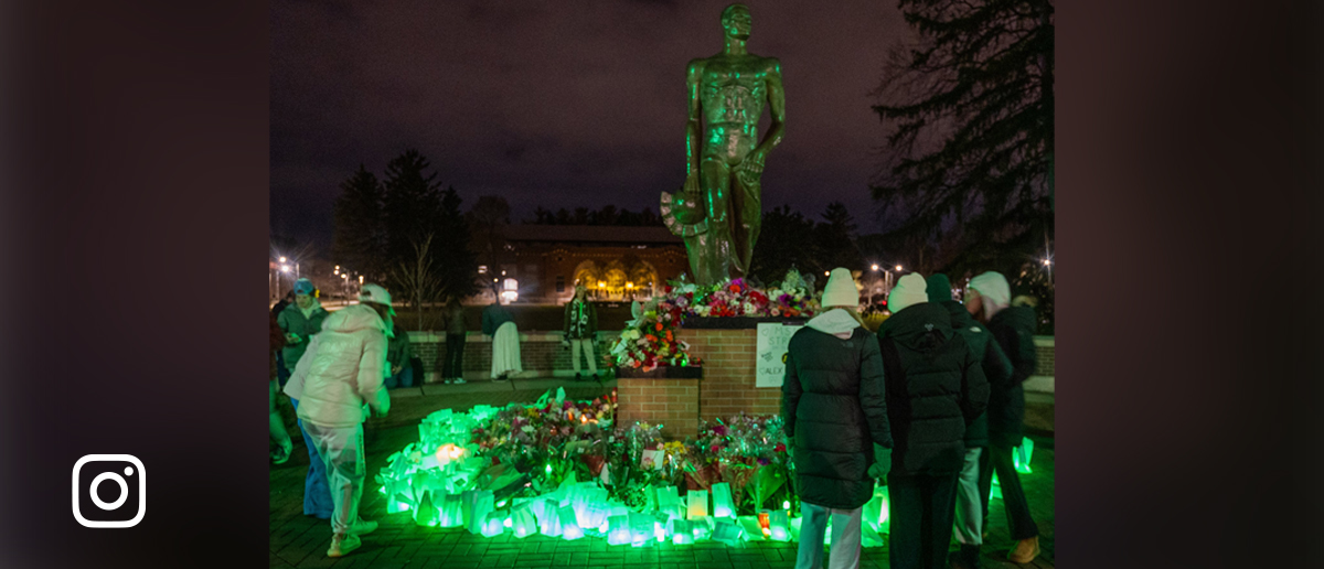 The Spartan statue is surrounded by fresh flowers and green luminaries on the night of Feb. 13, 2024