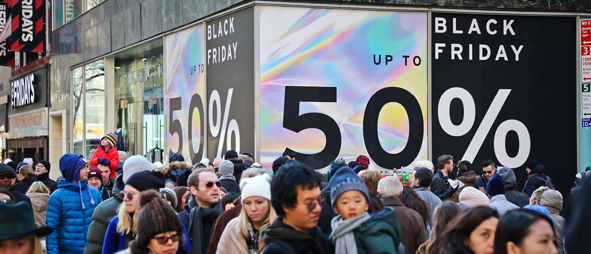 Shoppers walk past signs saying Black Friday, Up to 50% Off