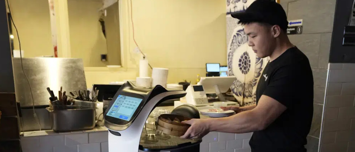 A restaurant worker places a meal onto a robot server to be delivered to a customer