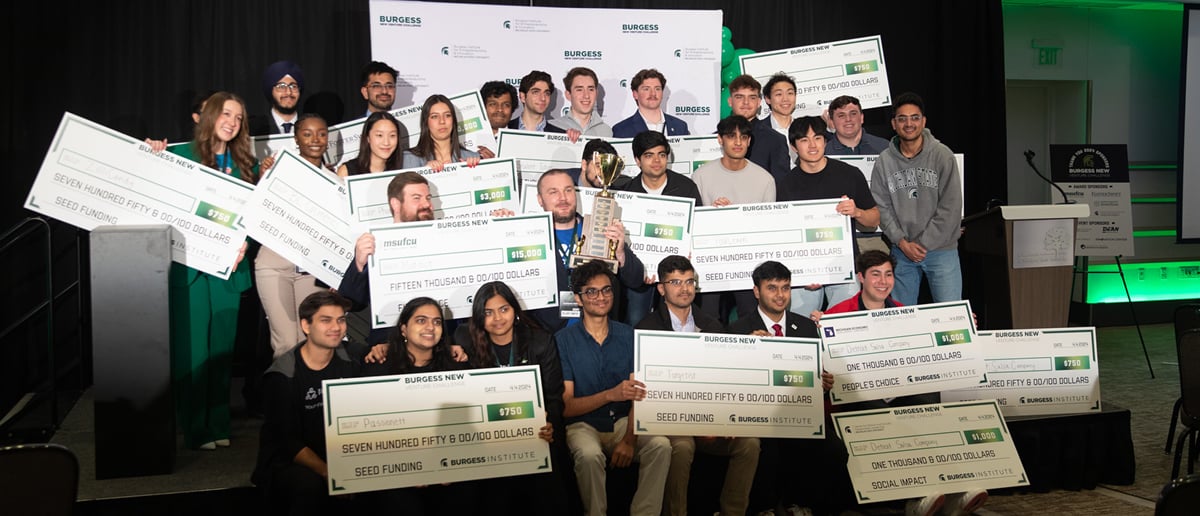 Students from 15 startup teams pose with oversized checks and a trophy