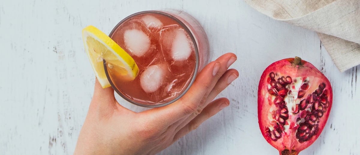 A glass of pinkish kombucha with ice and a twist of lemon