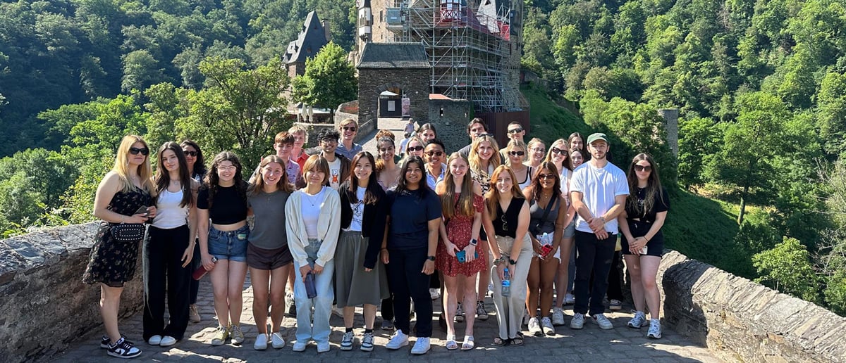 A large group of Broad students pose in front of a castle in Europe