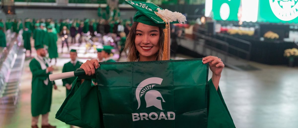 A graduate holding up a Broad flag after commencement