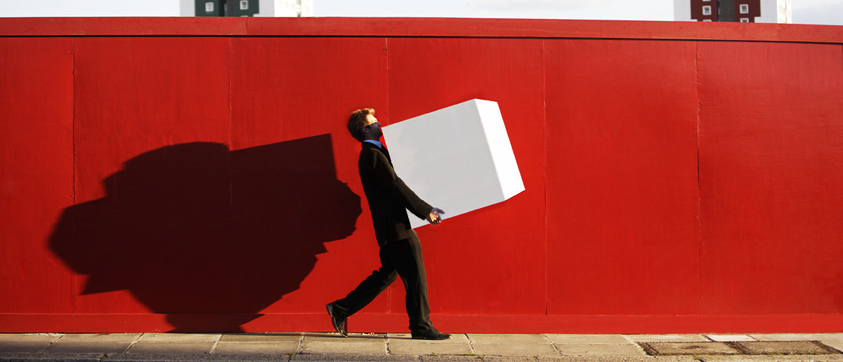 A man in a suit carries a large white box down a sidewalk